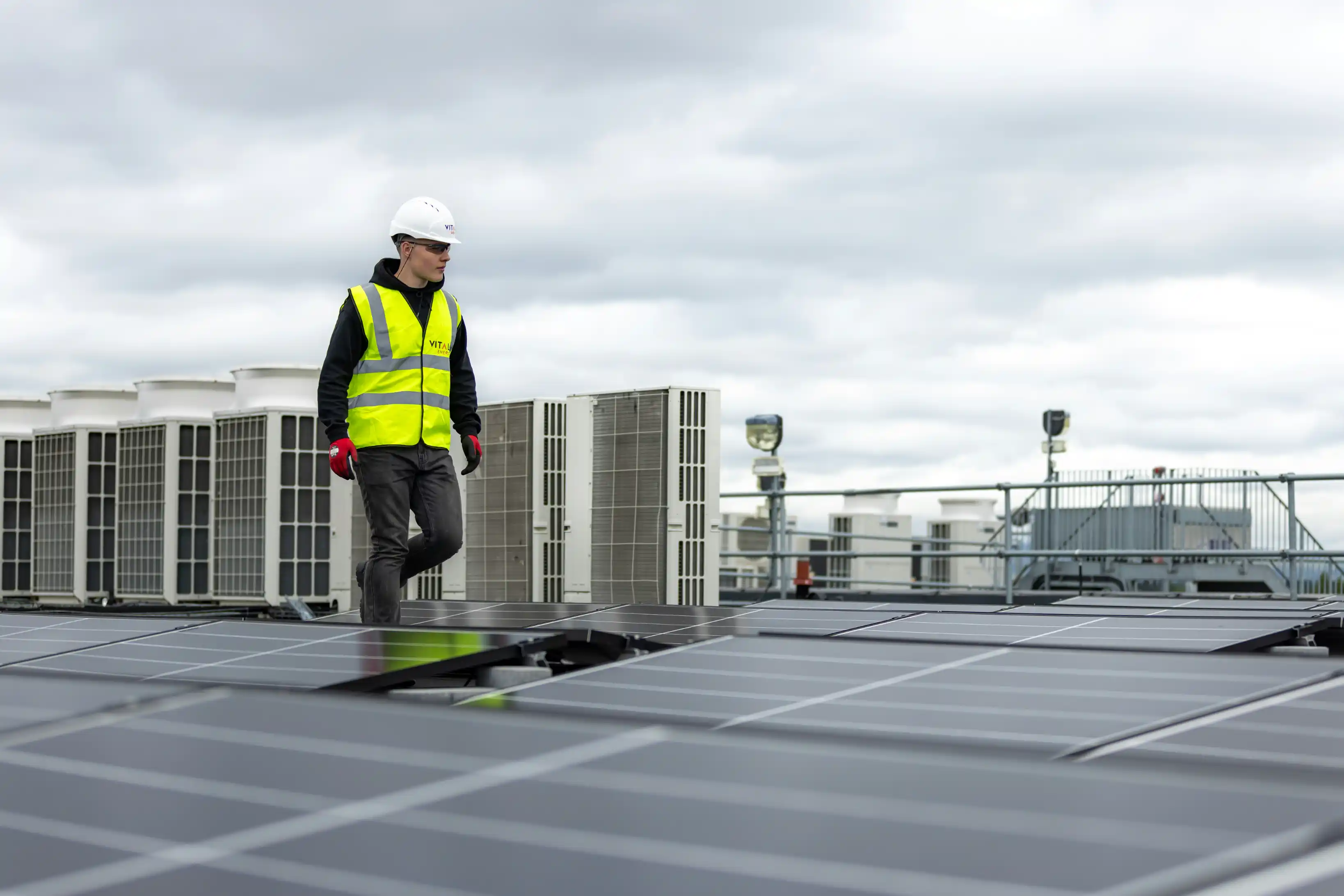 A technician in a high-visibility vest checking equipment on a commercial rooftop