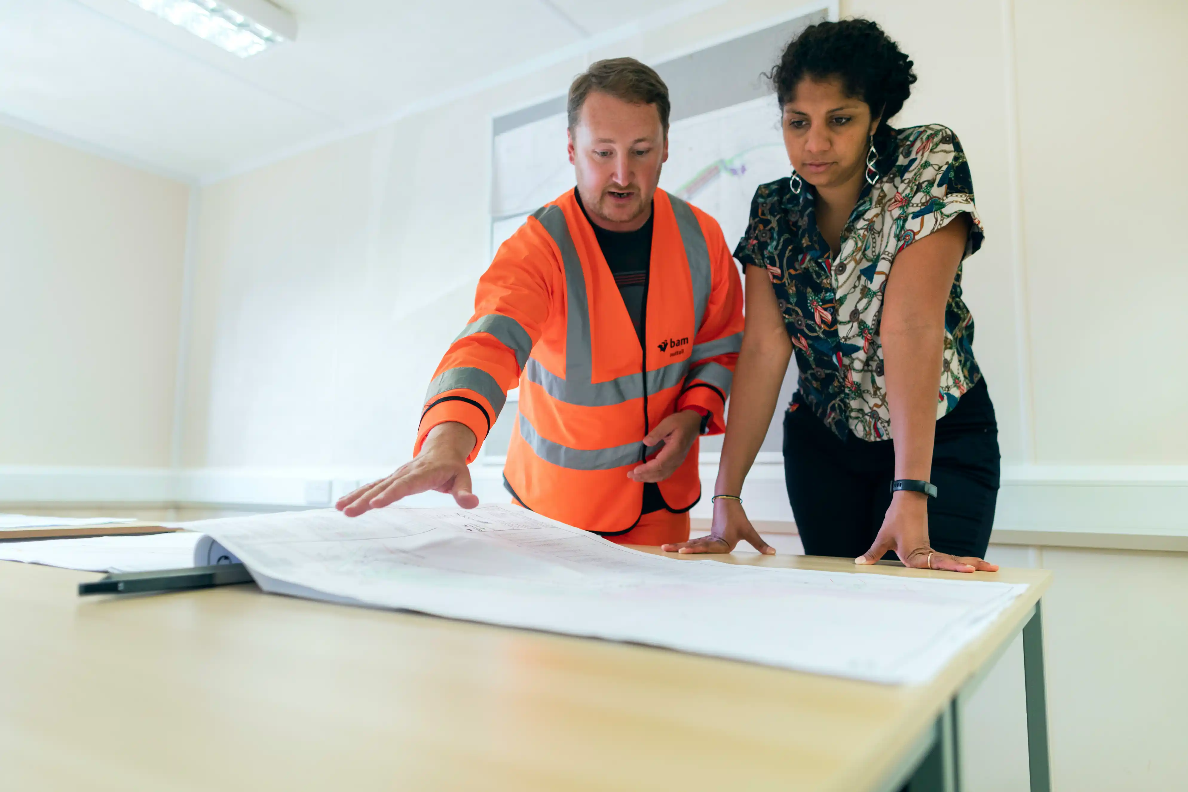 A construction lead in a high-visibility jacket reviewing plans with a colleague