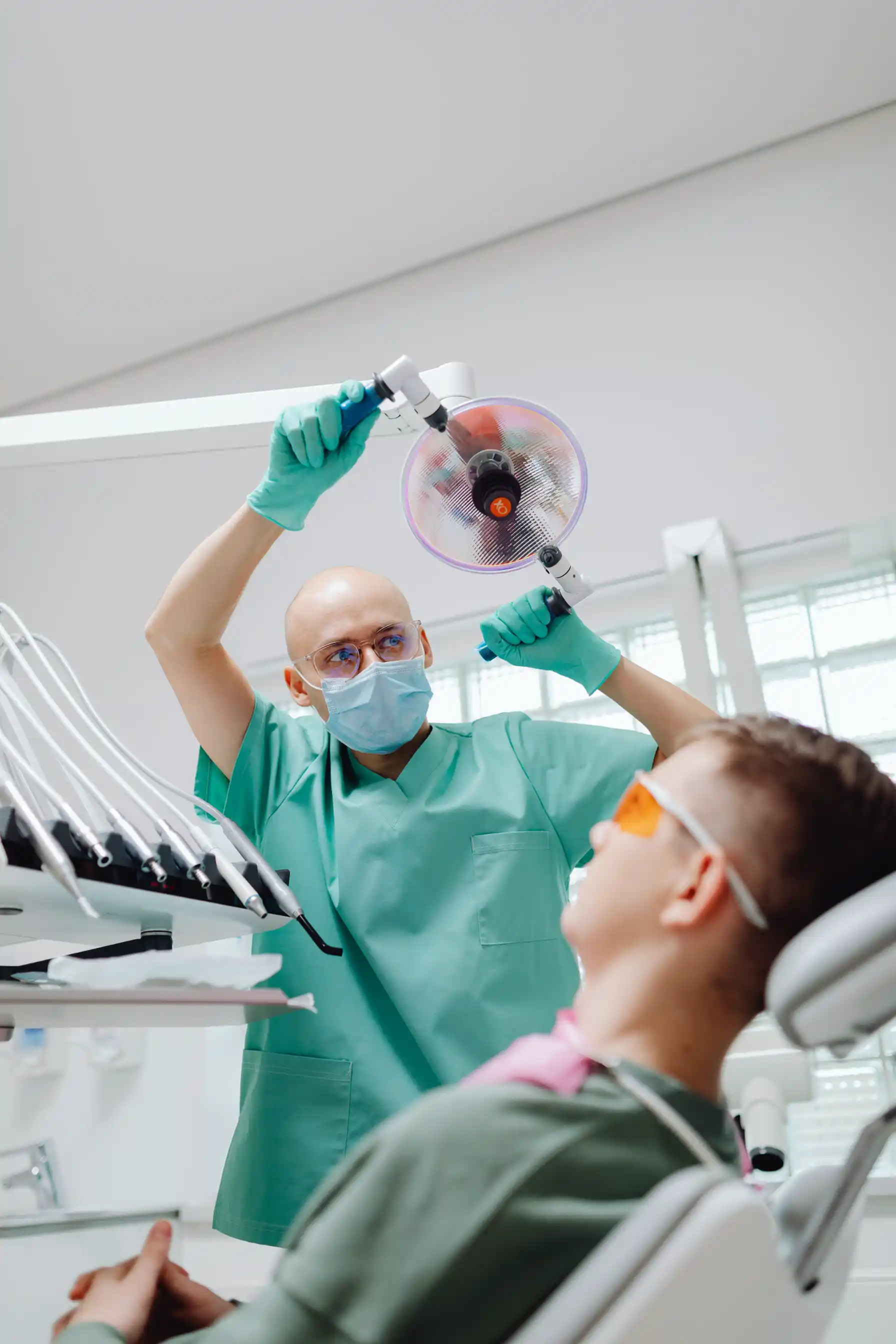 A dental hygienist in scrubs and a mask cleaning a patient's teeth