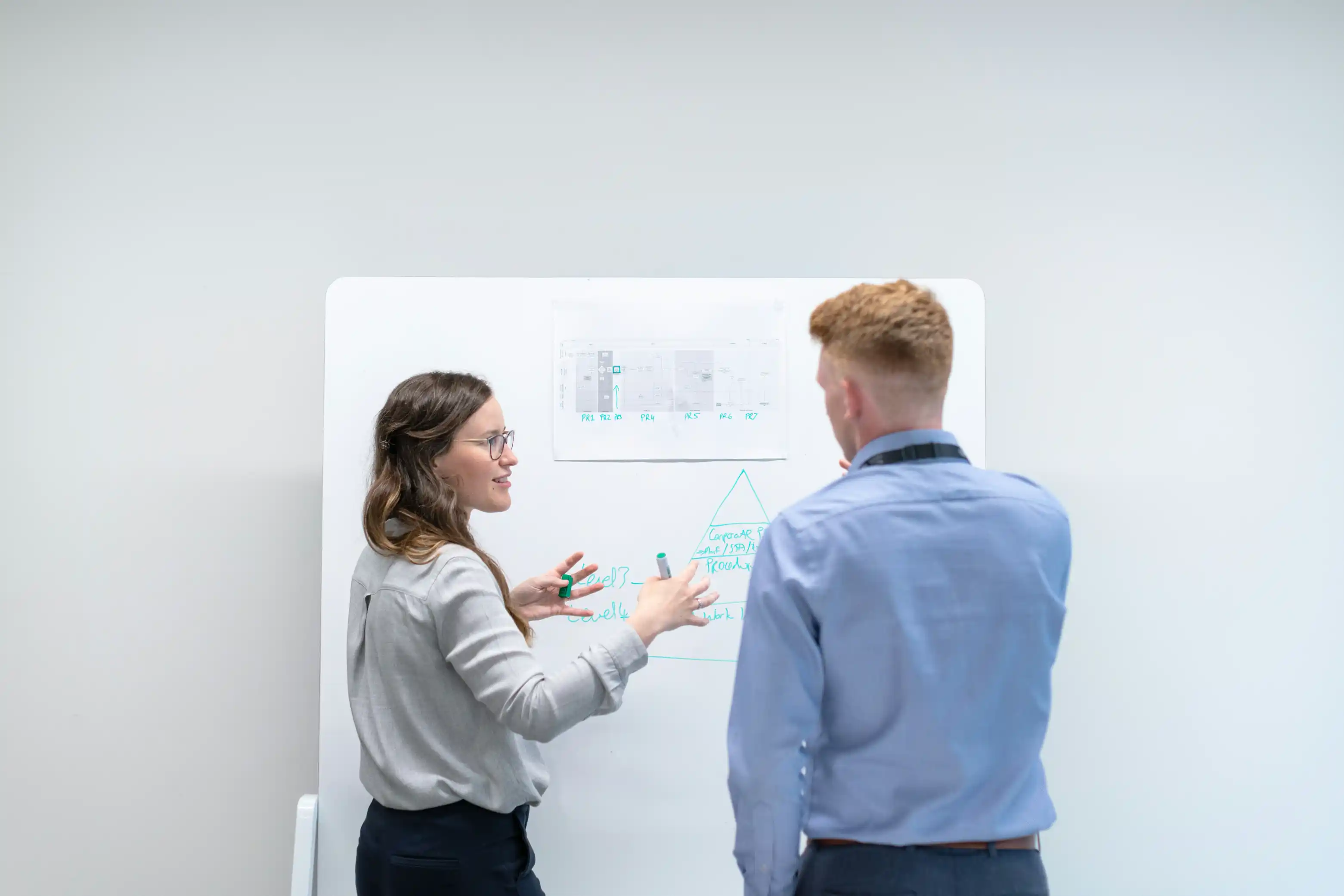 Two engineers discussing a technical sketch at a whiteboard