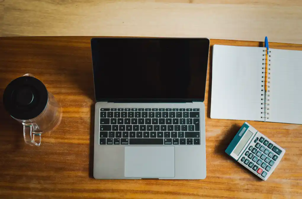 A laptop, notebook and calculator on a wooden desk