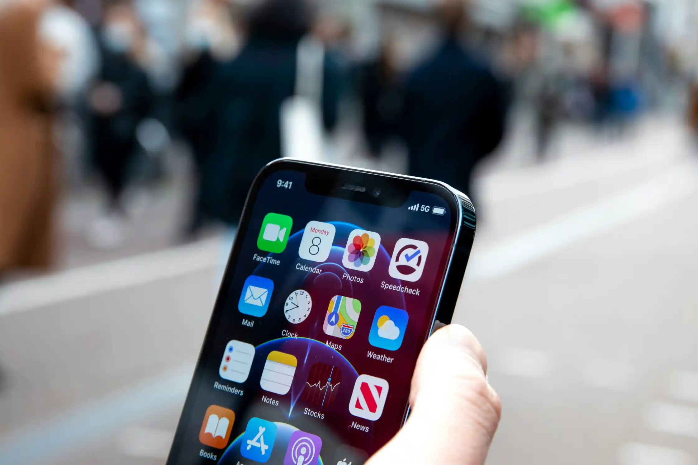 A hand holding a smartphone with apps on screen in a busy street